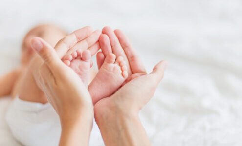 Mother holds newborn baby's bare feet. Tiny feet in woman's hand.